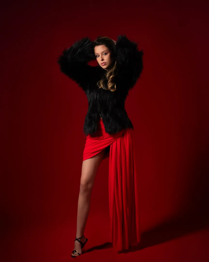Ensaio de moda com casaco preto de pelúcia e saia vermelha sobre fundo vermelho
